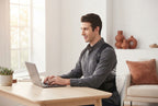 A person wearing a posture corrector belt while working at a desk in a bright, modern, terracotta-accented office.